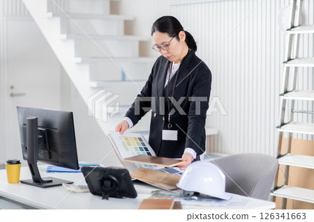 A female employee of a construction company working while spreading out building materials and documents A female employee of a construction company working while spreading out building materials and documents 126341663