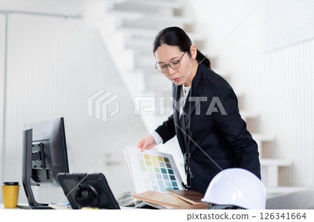 A female employee of a construction company working while spreading out building materials and documents A female employee of a construction company working while spreading out building materials and documents 126341664