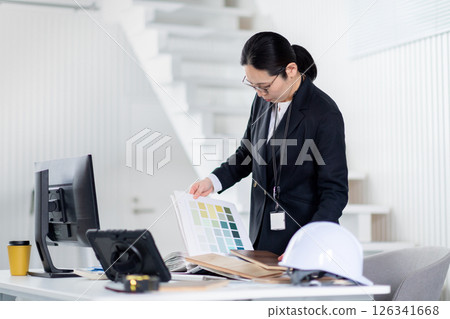 A female employee of a construction company working while spreading out building materials and documents A female employee of a construction company working while spreading out building materials and documents 126341668