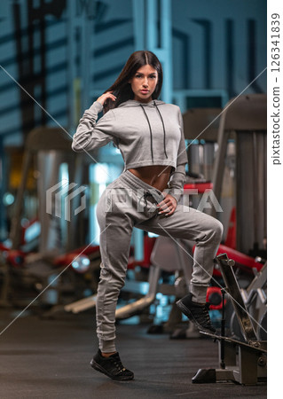 fitness enthusiast stands confidently in a gym dressed in stylish workout attire. The setting features various gym equipment and vibrant lighting creating an energetic atmosphere. 126341839
