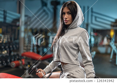 dedicated individual in a grey workout outfit exercises in a modern gym. The atmosphere is intense with gym equipment and vibrant lighting enhancing the focus on fitness. 126341942