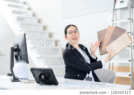 A female employee of a house manufacturer explaining with a sample of flooring 126342317
