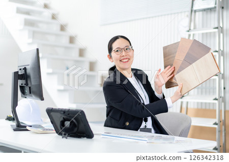 A female employee of a house manufacturer explaining with a sample of flooring A female employee of a house manufacturer explaining with a sample of flooring 126342318