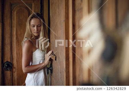 Young woman in white dress inside luxury villa. Girl relaxing on family summer vacation. Tropical lifestyle. Young woman in white dress inside luxury villa. Girl relaxing on family summer vacation. Tropical lifestyle. 126342829