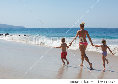 Happy family - mother, kids hold hands and run with fun along edge of sunset sea on sand beach. Active parents and people outdoor activity on tropical summer vacations with children 126342832