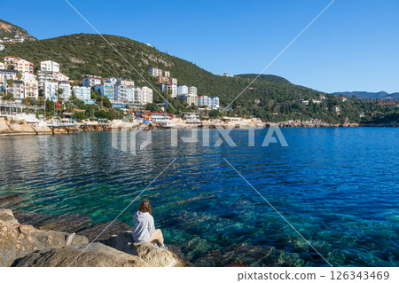 Woman looking at sea and historical town Kash placed on hills by coast of mediterranean sea in Antalya region in Turkey. Capturing summer vacation, popular place for family travel with kids. Woman looking at sea and historical town Kash placed on hills by coast of mediterranean sea in Antalya region in Turkey. Capturing summer vacation, popular place for family travel with kids. 126343469