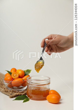 Kumquat fruits in glass bowl, jar with jam and spoon in hand on white background 126344004