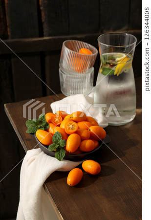 Fresh kumquat fruits in pan, glasses and towel on table on wooden background Fresh kumquat fruits in pan, glasses and towel on table on wooden background 126344008