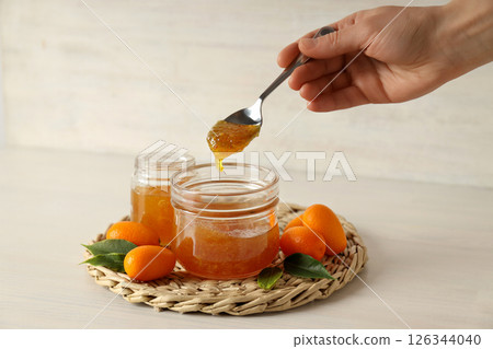 Kumquat fruits, jars with jam  and spoon in hand on light background 126344040