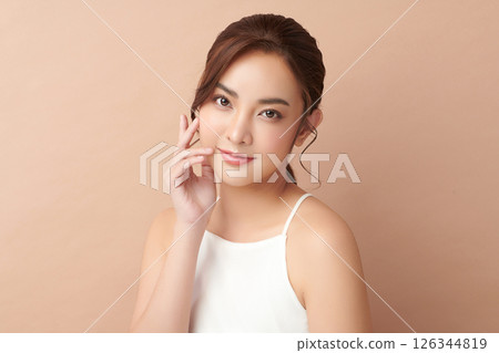 A beautiful young Asian woman with clean, fresh skin against a beige background. Skincare, facial treatment, cosmetology, beauty, and spa. An elegant portrait of an Asian woman. 126344819