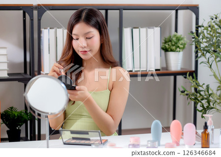 Happy young asian woman applying makeup with a brush on cheek looking mirror. Happy young asian woman applying makeup with a brush on cheek looking mirror. 126346684