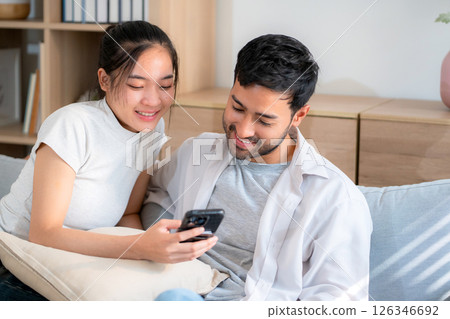 Young asian couple relax sitting on sofa looking smartphone together in living room at home. Young asian couple relax sitting on sofa looking smartphone together in living room at home. 126346692