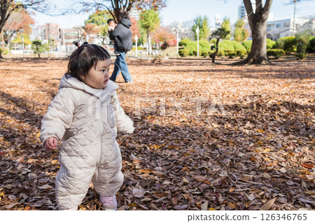 [一名 1 歲的孩子站在落葉覆蓋的冬季公園玩耍] 126346765