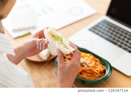 中年婦女在辦公室的辦公桌上吃三明治和義大利麵午餐 中年婦女在辦公室的辦公桌上吃三明治和義大利麵午餐 126347134