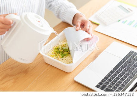 一位中年婦女在辦公室的辦公桌上做杯麵 一位中年婦女在辦公室的辦公桌上做杯麵 126347138
