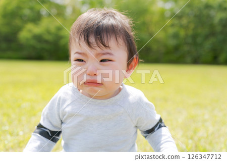 Baby sitting on the grass and crying 126347712