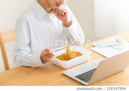 A middle-aged woman worries while eating instant yakisoba noodles at her desk in the office 126347804