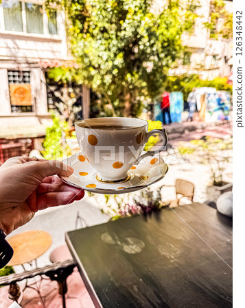Coffee cup with polka dots held in hand against a lively outdoor cafe backdrop. High quality photo 126348442