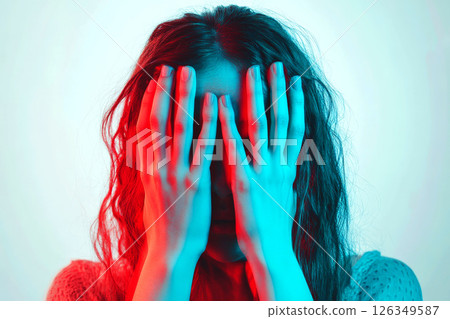 An individual covers their face with both hands, conveying a sense of distress or emotional turbulence, depicted in a close-up shot focusing on the hands and partial expression. 126349587