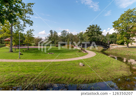 Scenic park with a curved path, a bridge, and green landscaping on a sunny day Scenic park with a curved path, a bridge, and green landscaping on a sunny day 126350207