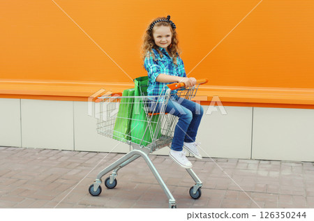 Happy little girl child with trolley cart and colorful shopping bags on city street Happy little girl child with trolley cart and colorful shopping bags on city street 126350244
