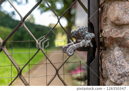 An ornate metal gate handle opens to a lush garden pathway on a sunny day in summer An ornate metal gate handle opens to a lush garden pathway on a sunny day in summer 126350347