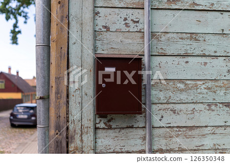 A brown mailbox attached to the weathered wood wall of a quaint house in a quiet neighborhood during the daytime A brown mailbox attached to the weathered wood wall of a quaint house in a quiet neighborhood during the daytime 126350348