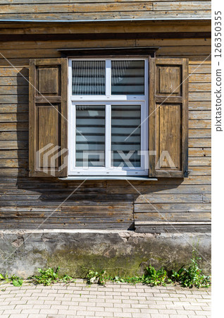 A wooden window with shutters opens to a rustic exterior of a house on a sunny day 126350355