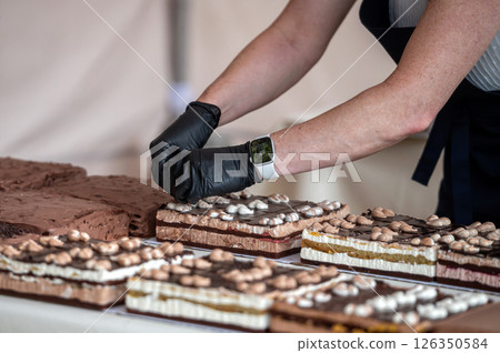 Baker decorating chocolate cakes with whipped cream. Shallow depth of feld Baker decorating chocolate cakes with whipped cream. Shallow depth of feld 126350584