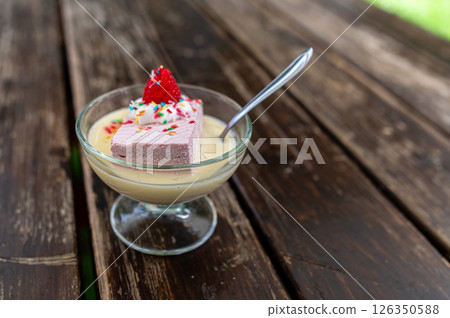 Dessert served in a glass bowl featuring a slice of pink mousse topped with a strawberry on a wooden table Dessert served in a glass bowl featuring a slice of pink mousse topped with a strawberry on a wooden table 126350588