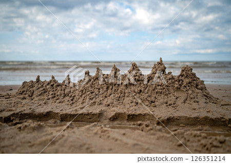A sandcastle stands on the shore as waves gently lap at its base. 126351214
