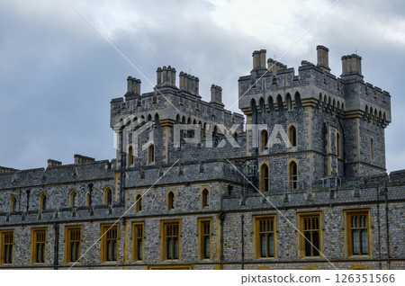 Close-up view of Windsor Castle's upper towers in England, showcasing historic stone architecture and medieval details under a dramatic cloudy sky Close-up view of Windsor Castle's upper towers in England, showcasing historic stone architecture and medieval details under a dramatic cloudy sky 126351566