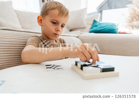 Child intently focuses on solving a puzzle at home, engaging in a cognitive and developmental activity. The scene captures concentration and determination in a relaxed home setting 126351578