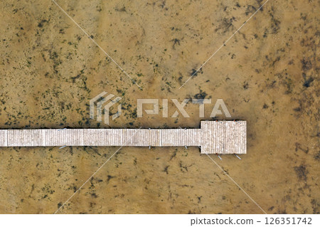 A wooden pier stretches over a calm lake, bordered by marshy terrain. A wooden pier stretches over a calm lake, bordered by marshy terrain. 126351742