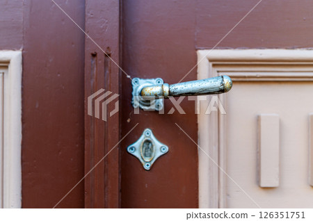 A close-up of an ornate door handle on a brown wooden door in a historic building A close-up of an ornate door handle on a brown wooden door in a historic building 126351751