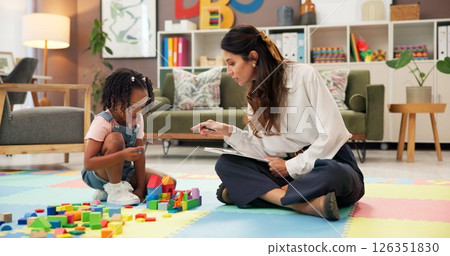 Therapist, woman and girl with clipboard, blocks and talk for evaluation, assessment or exam on floor. Person, psychologist and child with toys, advice and checklist for notes with point at clinic 126351830