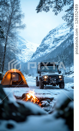 Firelight glows as lone camper faces cold night beside off-road truck and tent, braving deep snow and fierce wind in a bold wild camp adventure 126352489
