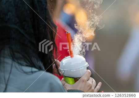 A person holds a steamy beverage topped with fog in a vibrant outdoor setting 126352660
