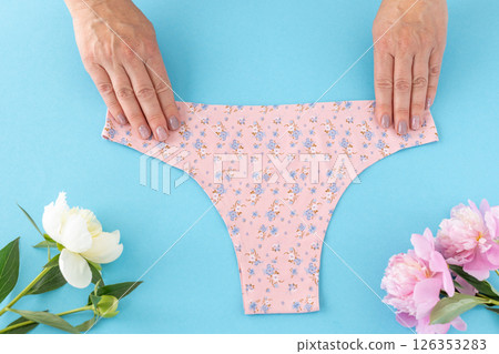 Women's hands with a pink panties on the blue background. 126353283