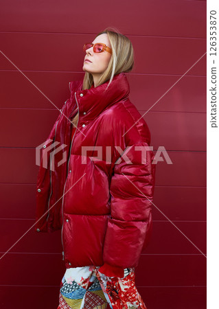 High fashion photo of a young blond woman in red glossy down jacket, poloneck, and pants. Monochrome trendy red outfit. High fashion photo of a young blond woman in red glossy down jacket, poloneck, and pants. Monochrome trendy red outfit. 126353870