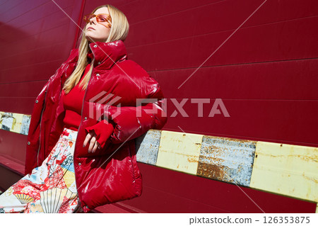 High fashion photo of a young blond woman in red glossy down jacket, poloneck, and pants. Monochrome trendy red outfit. High fashion photo of a young blond woman in red glossy down jacket, poloneck, and pants. Monochrome trendy red outfit. 126353875