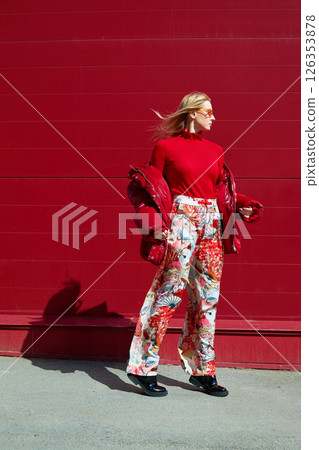 High fashion photo of a young blond woman in red glossy down jacket, poloneck, and pants. Monochrome trendy red outfit. High fashion photo of a young blond woman in red glossy down jacket, poloneck, and pants. Monochrome trendy red outfit. 126353878