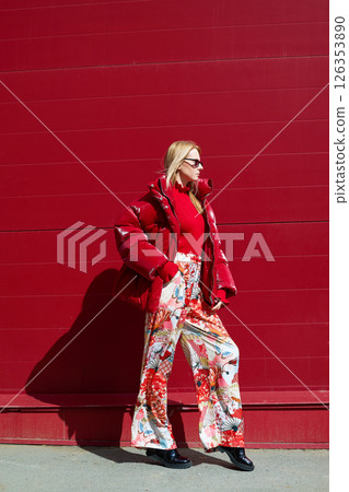 High fashion photo of a young blond woman in red glossy down jacket, poloneck, and pants. Monochrome trendy red outfit. High fashion photo of a young blond woman in red glossy down jacket, poloneck, and pants. Monochrome trendy red outfit. 126353890