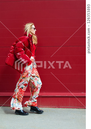 High fashion photo of a young blond woman in red glossy down jacket, poloneck, and pants. Monochrome trendy red outfit. High fashion photo of a young blond woman in red glossy down jacket, poloneck, and pants. Monochrome trendy red outfit. 126353893