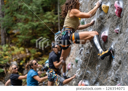 Woman with prosthetic leg demonstrates strength and resilience while rock climbing with a group in a natural setting 126354071