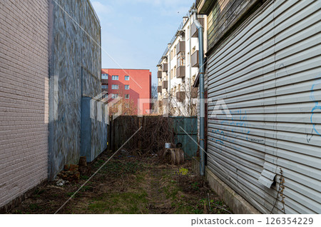 Narrow alleyway between buildings with overgrown vegetation and distant residential view Narrow alleyway between buildings with overgrown vegetation and distant residential view 126354229