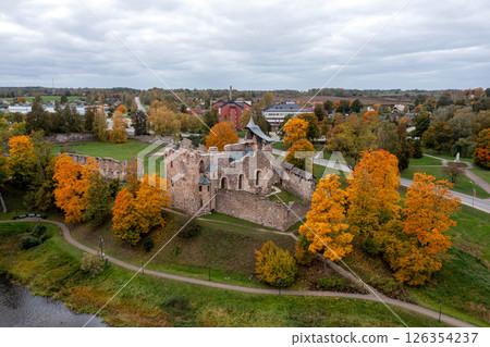 An ancient castle sits amid colorful autumn trees near a calm waterfront in Latvia. 126354237