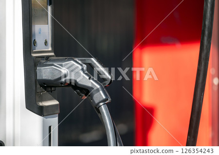 An electric vehicle connects to a charger in a bustling city during bright daylight. An electric vehicle connects to a charger in a bustling city during bright daylight. 126354243