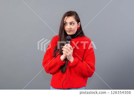 young, emotional brunette with a microphone dressed in a red sweater sings karaoke or says a speech 126354308