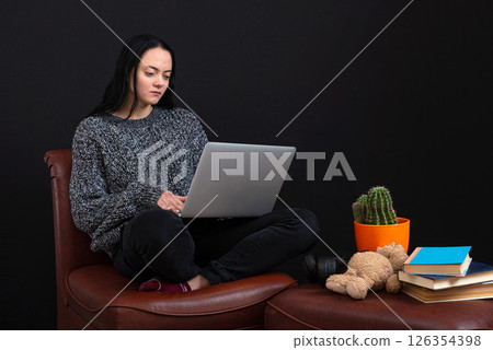 focused young freelance woman sitting with laptop and headphones, working remotely online from home 126354398